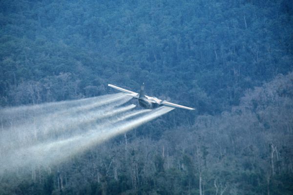Us military transport plane spraying agent orange over forest.